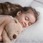 Малко момиче спи, гушнало плюшеното си мече