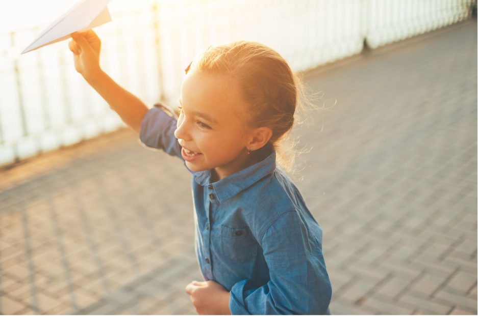 Момиче тича навън на слънце и държи хартиен самолет